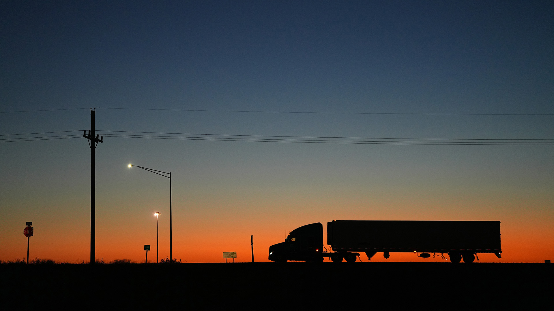 Silhouette of a semi truck driving on a rural road at sunset