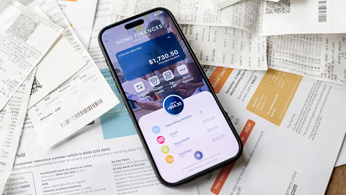 Smartphone sitting on various paper bills displaying a budgeting app